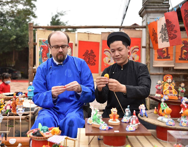 A foreign traveler is learning to make To he folk toy in Duong Lam ancient village. Hanoi Times Photo: Khanh Huy